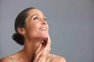 Confident mature woman with smooth skin posing in a studio against a gray background, reflecting the results of anti-aging treatment and enhanced collagen from professional dermatology care