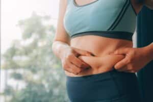 Overweight woman measuring her abdomen, highlighting persistent abdominal fat that may not respond to diet and exercise