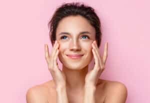 Beautiful woman with glowing, clear skin against pink background, representing results of hydrafacial treatment and advanced skin care.