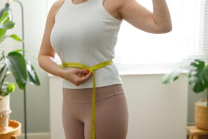 Woman measuring waist with tape to track fitness progress and weight loss results. Woman measuring waist with tape to track fitness progress and weight loss results.