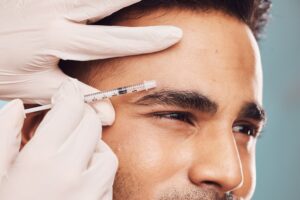 Close-up of man receiving Botox injection near eyebrow in studio, concept of skincare, anti-aging facial filler, and cosmetic treatment. Close-up of man receiving Botox injection near eyebrow in studio, concept of skincare, anti-aging facial filler, and cosmetic treatment.