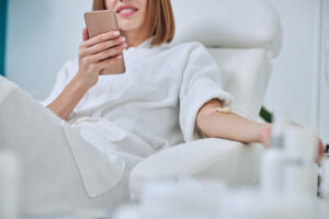 Woman relaxing and scrolling on her phone while receiving IV Therapy for improved energy and wellness.
